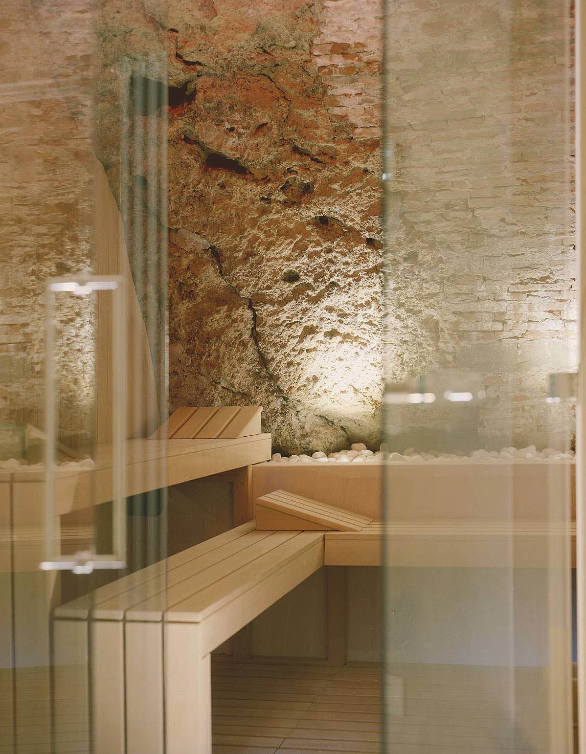 Sauna interior with exposed stone feature wall, glass front and pale timber benches